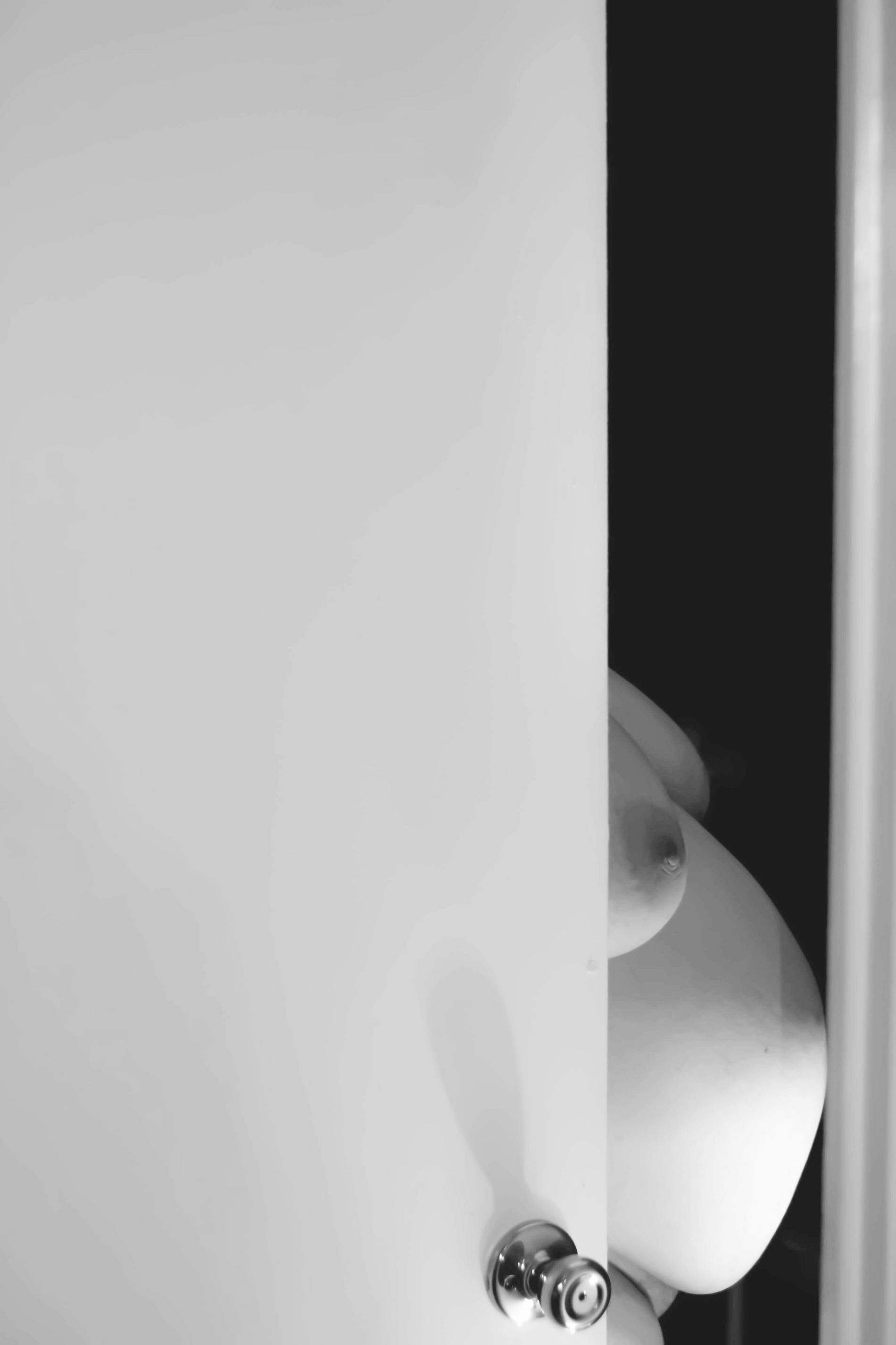 Black-and-white artistic maternity portrait framed by a partially open door