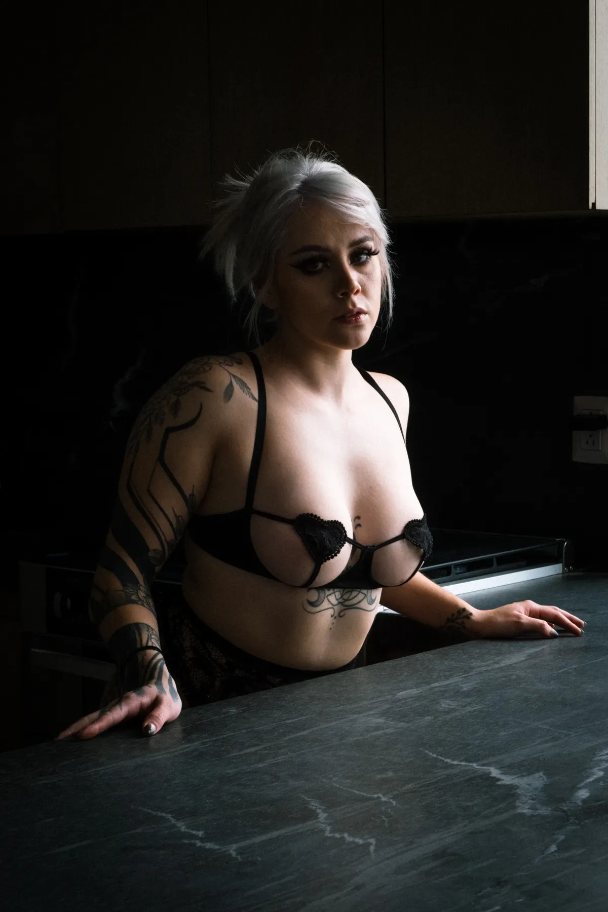 Tattooed woman posing confidently in black lingerie in a dark interior